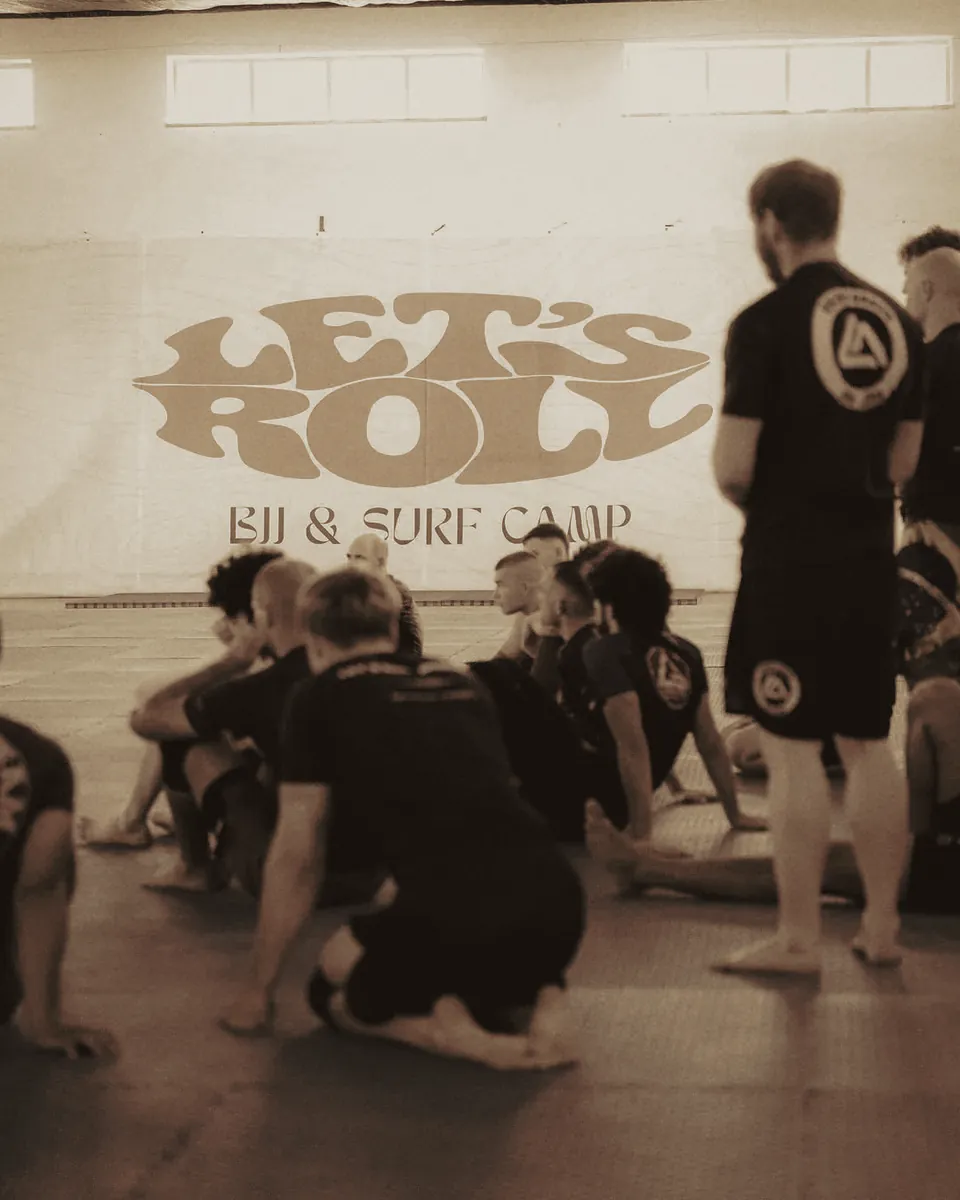 Teilnehmende im Kreis vor dem Banner des BJJ & Surf Camps.