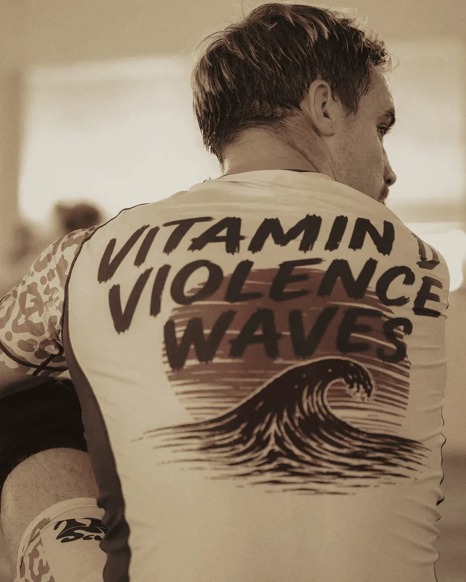 Camp-Rashguard mit Rückenprint „Vitamin D, Violence, Waves“.