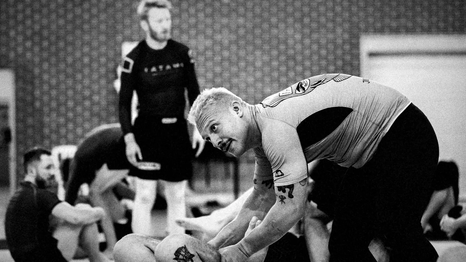 Coach zeigt eine Grappling-Position am Boden, die Gruppe schaut zu.