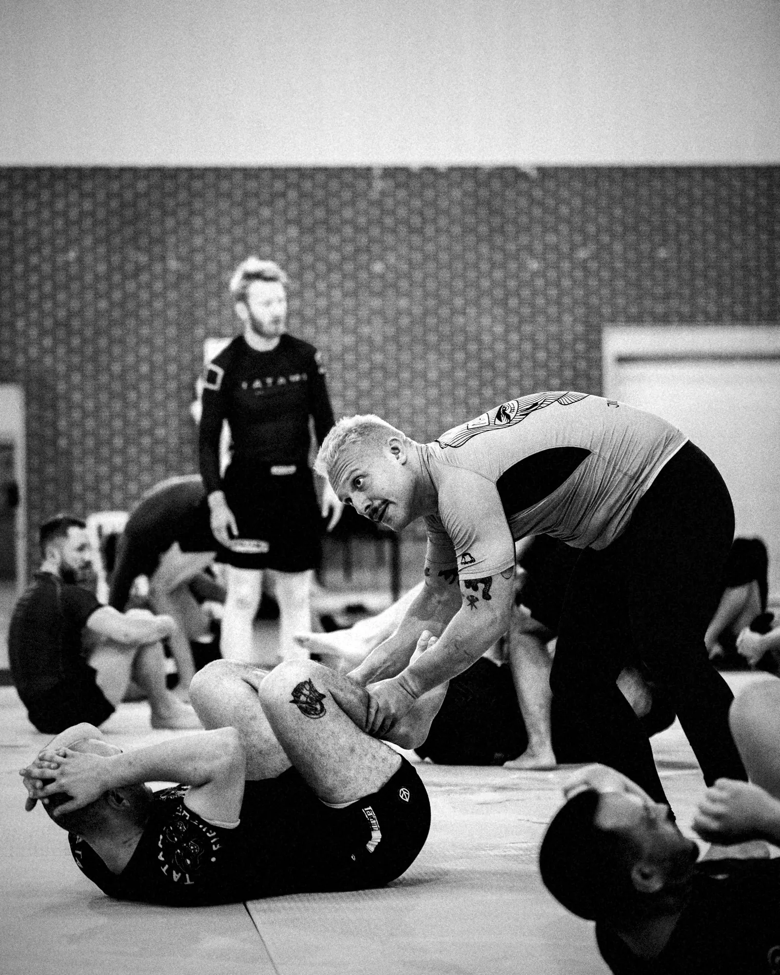 Coach zeigt eine Grappling-Position am Boden, die Gruppe schaut zu.